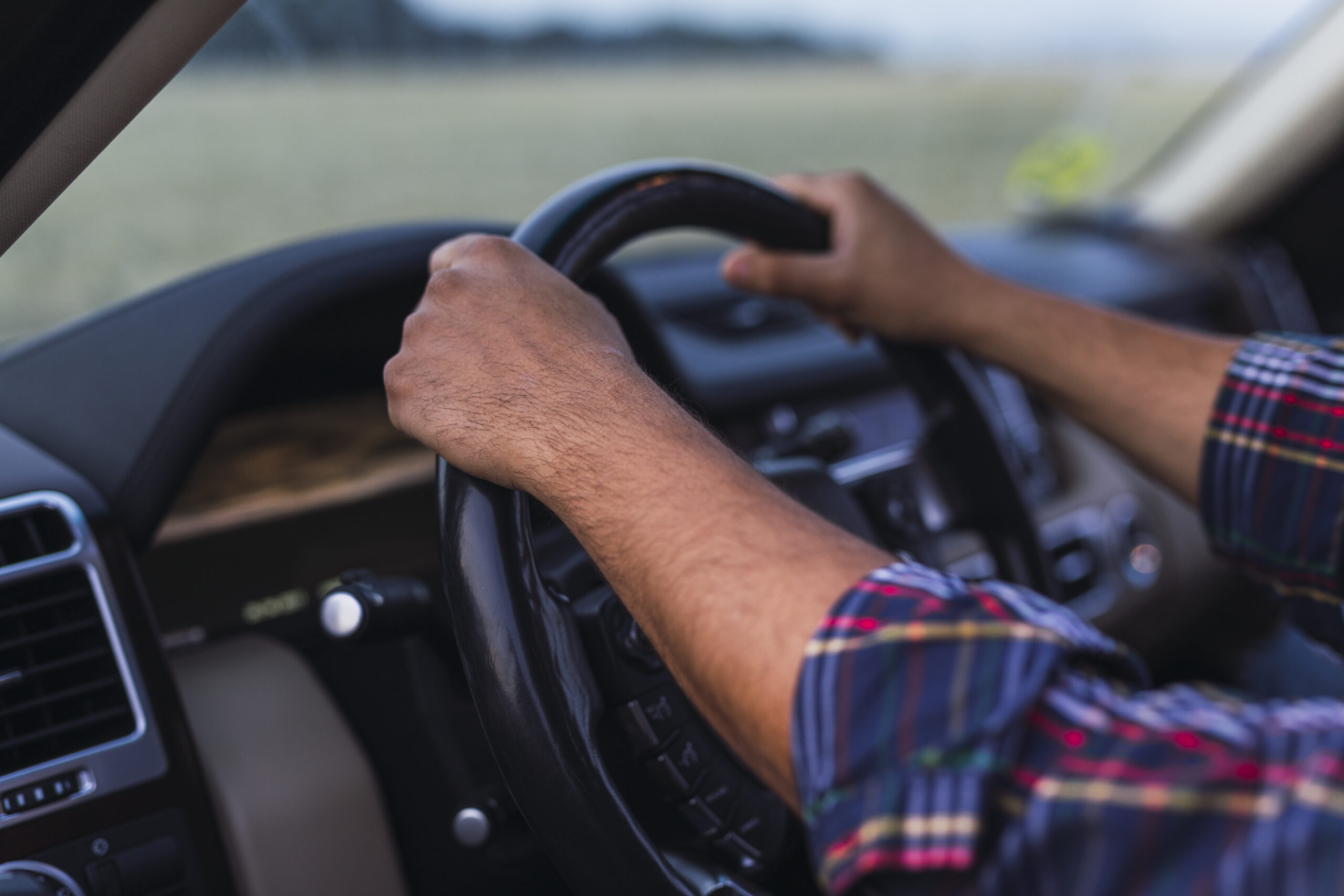 A photo of a person’s hands on a steering wheel of a car