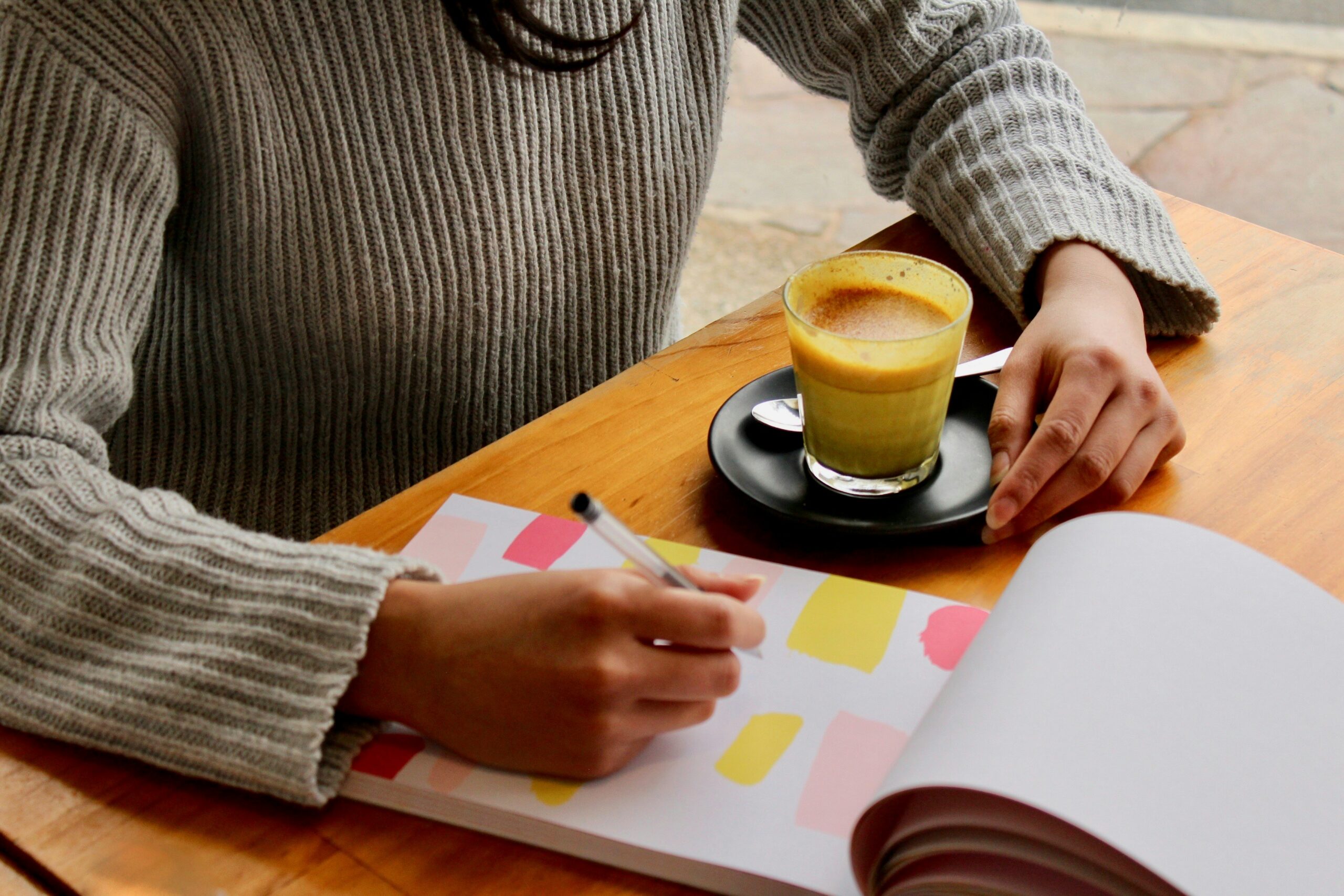 A person writing a document with coffee on the table